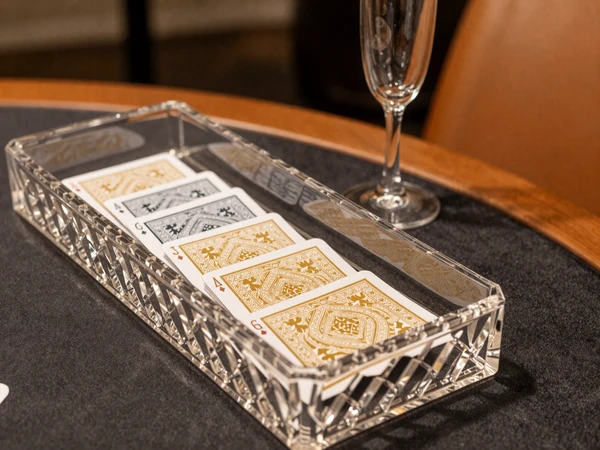 Eleganter Baccarat-Tisch mit Kristallschuh, goldverzierten Karten und Kristallchampagnerglas in luxuri&ouml;sem dunklem Setting